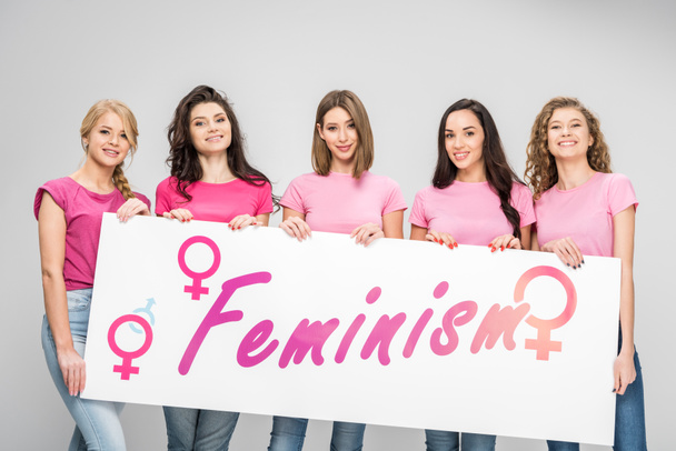 cheerful girls holding large sign with feminism lettering isolated on grey - Photo, Image