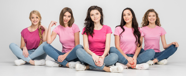 cheerful young women sitting on floor and smiling on grey background - Photo, Image