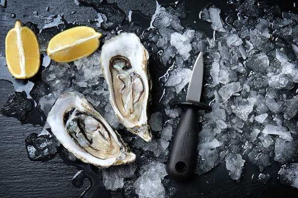 Tasty raw oysters with ice and lemon on dark background - Photo, Image