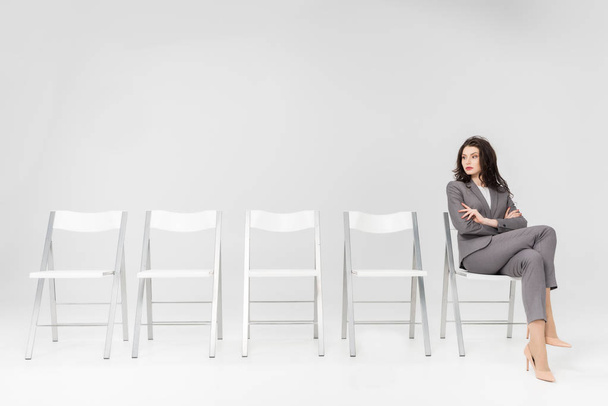 αυτοπεποίθηση γυναίκα κάθεται με σταυρωμένα χέρια και σταυρωμένα τα πόδια στην καρέκλα που απομονώνονται σε γκρι - Φωτογραφία, εικόνα