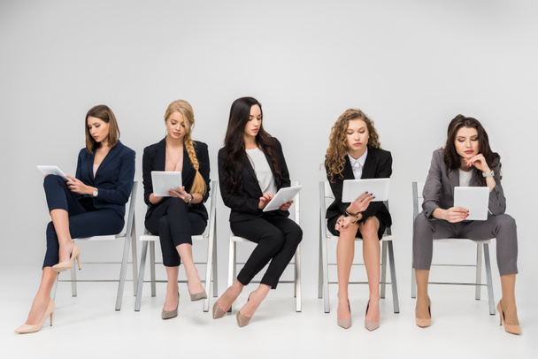 aantrekkelijke vrouwelijke ondernemers met behulp van digitale tabletten zittend op stoelen geïsoleerd op grijs - Foto, afbeelding