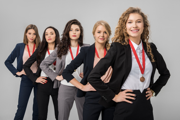 selectieve aandacht van vrolijke zakenvrouwen permanent met medailles geïsoleerd op grijs  - Foto, afbeelding
