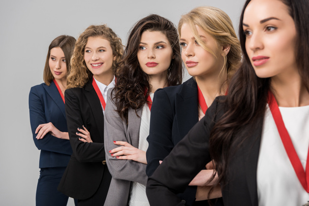 selective focus of beautiful young businesswomen standing with medals isolated on grey  - Foto, afbeelding