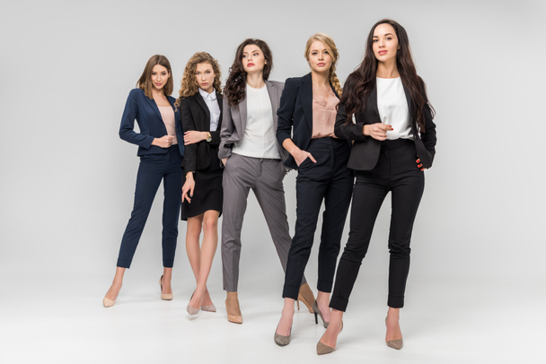 schöne erfolgreiche junge Frauen, die mit Händen in Taschen auf grauem Hintergrund stehen - Foto, Bild