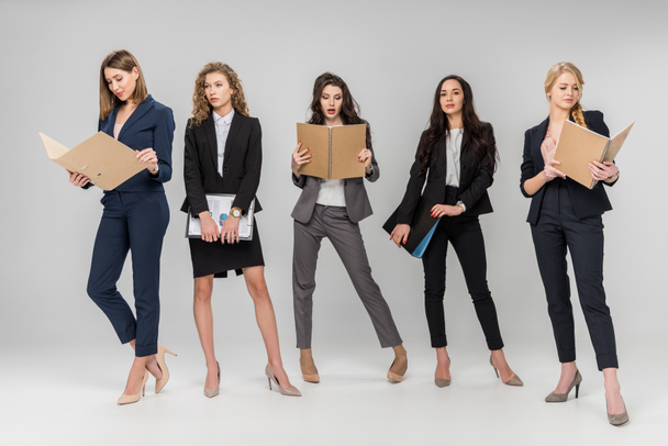 beautiful young businesswomen holding clipboards and folders while standing on grey background - Photo, Image