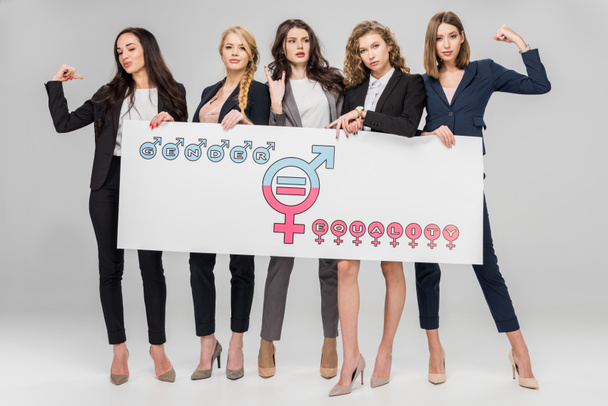 young businesswomen holding large sign with gender equality symbol on grey background - Photo, Image