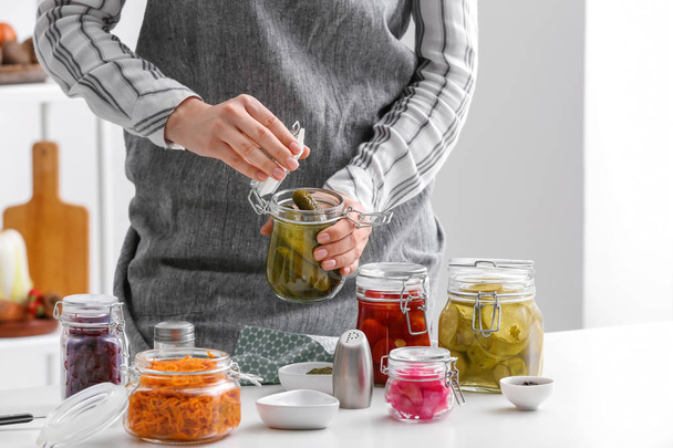 Женщина со стеклянной банкой ферментированных огурцов на кухне
 - Фото, изображение
