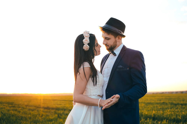 Romantic feelings in the field at sunset, the groom looks at the bride, the girl loves his boyfriend, the man is wearing a hat - Foto, imagen