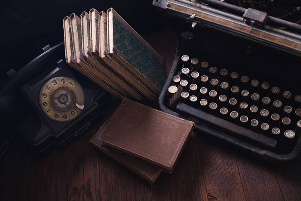 Старый ретро телефон со старинной пишущей машинкой и книгами на деревянном столе
 - Фото, изображение