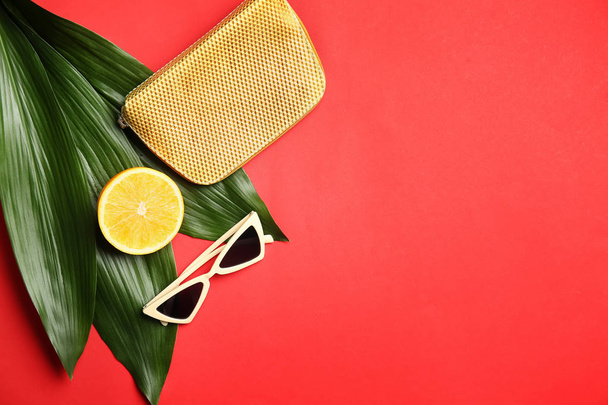 Elegantes gafas de sol con fruta naranja, bolsa y hojas tropicales sobre fondo de color
 - Foto, Imagen