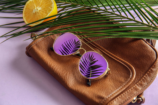 Stylish sunglasses with female bag and tropical leaves on color background - Φωτογραφία, εικόνα