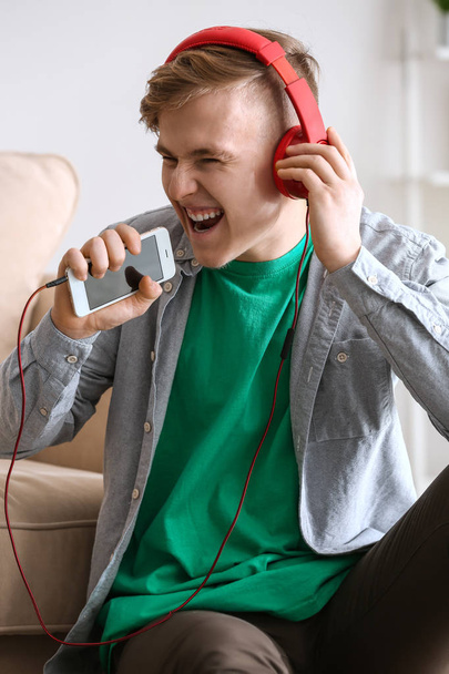 Handsome young man listening to music and singing at home - 写真・画像