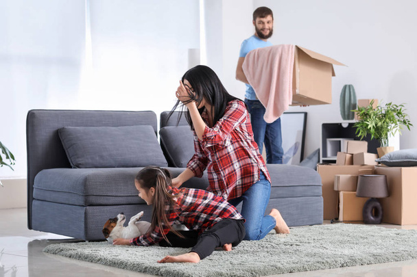 Woman and daughter playing with dog while man unpacking things after moving in new house - Фото, изображение
