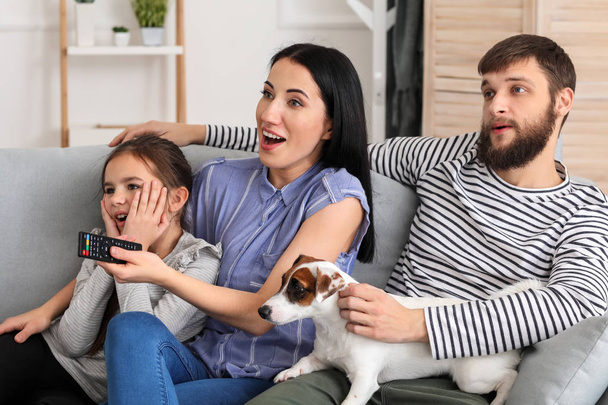 Семья смотрит телевизор, сидя дома на диване
 - Фото, изображение