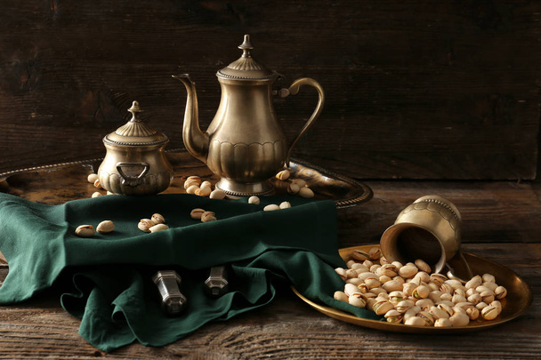 Вкусные фисташковые орехи с металлической посудой на деревянном столе
 - Фото, изображение