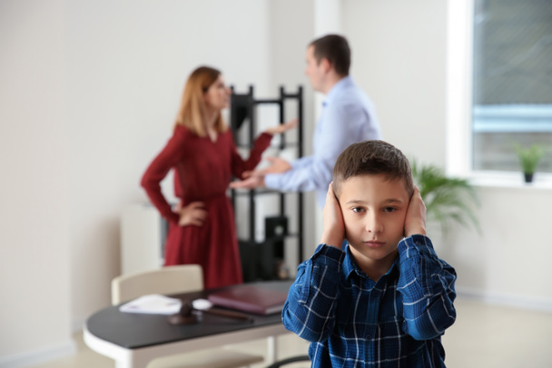 Грустный маленький мальчик со своими ссорящимися родителями в офисе адвоката. Концепция алиментов
 - Фото, изображение