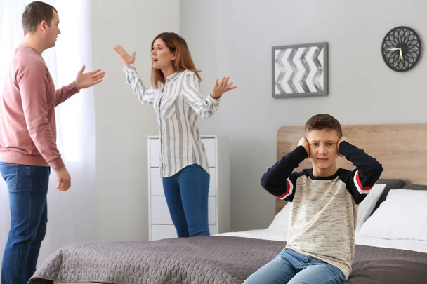 Грустный маленький мальчик закрывает уши, пока его родители спорят дома
 - Фото, изображение