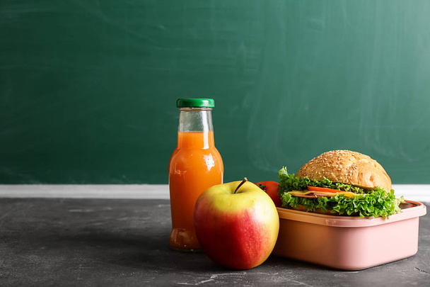 Scatola pranzo scuola con cibo gustoso e bottiglia di succo di frutta sul tavolo
 - Foto, immagini
