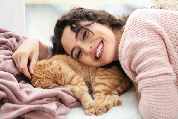 Young woman with cute funny cat near window - Foto, imagen
