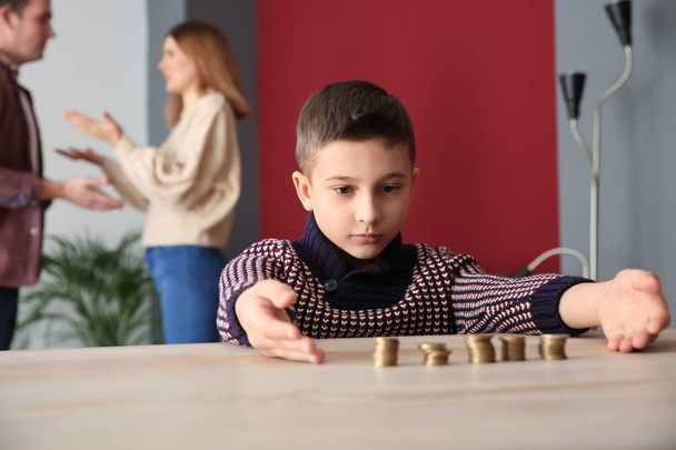 Sad little boy with coins and his quarreling parents at home. Concept of child support - Fotografie, Obrázek