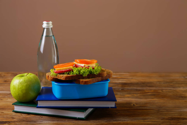 Шкільна обідня коробка зі смачною їжею та пляшкою води на столі
 - Фото, зображення