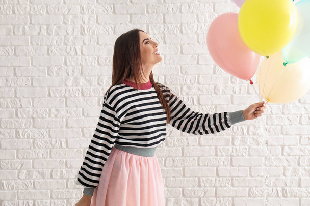 Mulher bonita com balões perto da parede de tijolo branco
 - Foto, Imagem