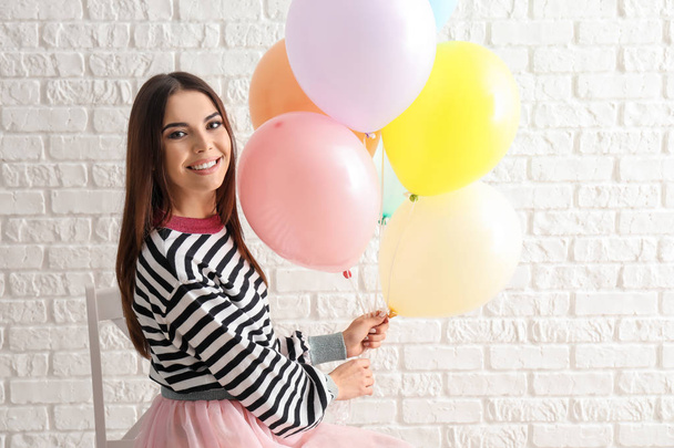 Beautiful young woman with balloons sitting on chair near white brick wall - Foto, immagini