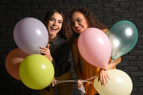 Όμορφες νεαρές γυναίκες με μπαλόνια κοντά σκοτεινό τούβλο τοίχο - Φωτογραφία, εικόνα