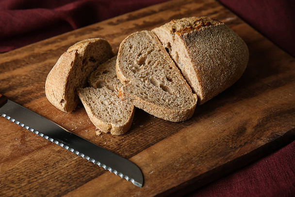 Cortar pan fresco con cuchillo sobre tabla de madera
 - Foto, imagen