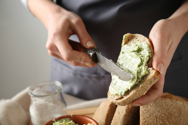 Mladá žena zelené másla na kus čerstvého chleba u stolu, closeup - Fotografie, Obrázek