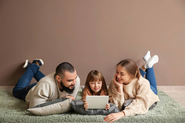 Ευτυχισμένη οικογένεια με υπολογιστή tablet ξαπλωμένος στο χαλί κοντά σε χρώμα τοίχου - Φωτογραφία, εικόνα