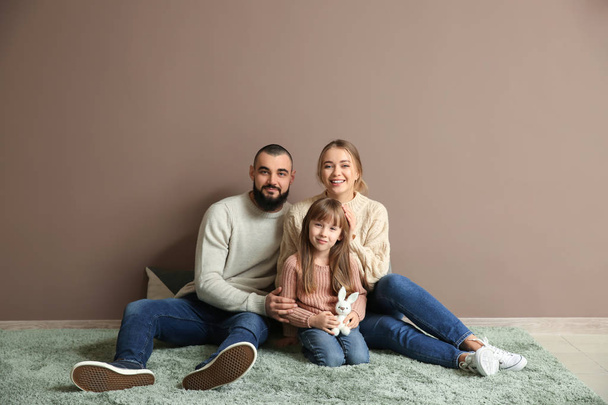 Szczęśliwa rodzina siedzi na dywanie w pobliżu kolor ściany - Zdjęcie, obraz