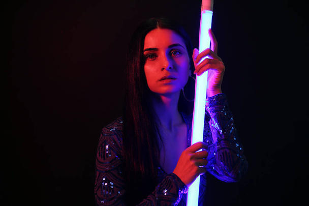 Portrait of beautiful young woman with neon lamp on dark background - Photo, Image