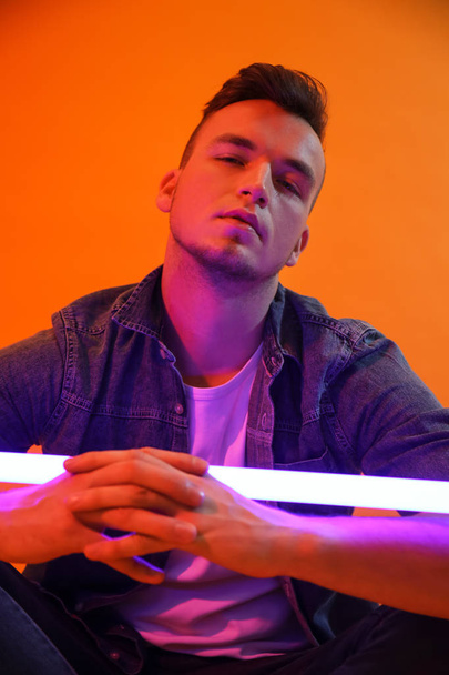 Toned portrait of handsome young man with neon lamp on color background - Foto, Imagen