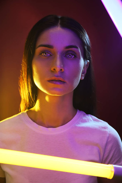 Toned portrait of beautiful young woman with neon lamp on dark background - Foto, Imagem