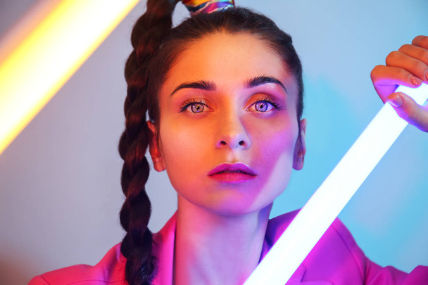 Toned portrait of beautiful young woman with neon lamp on color background - 写真・画像