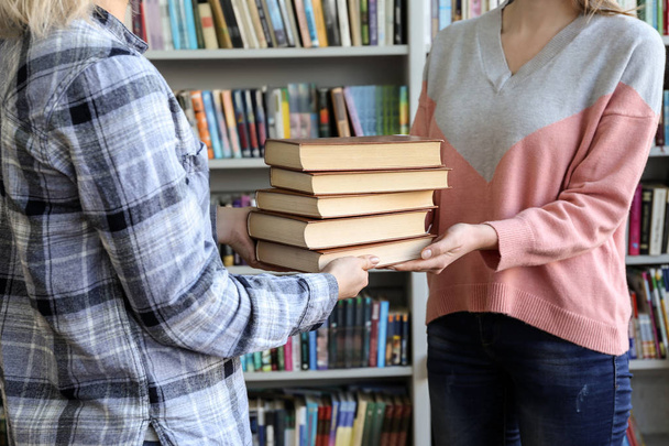 Young woman receiving books from librarian - Foto, imagen