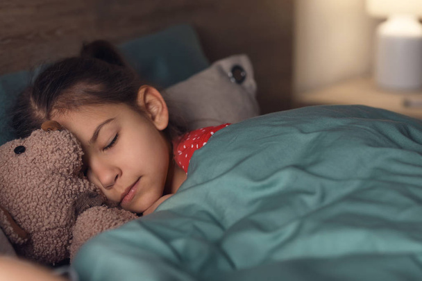 Cute sleeping girl with teddy bear in bed at home - Foto, afbeelding