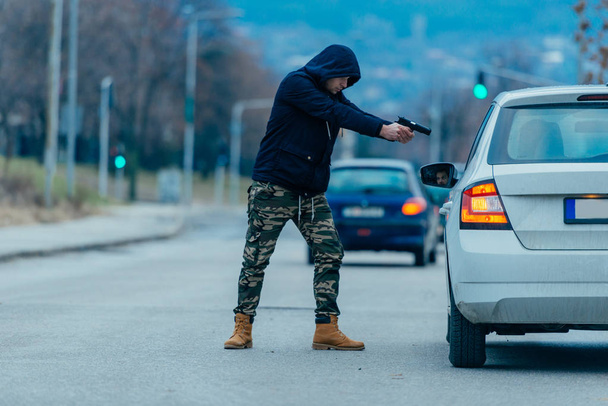 El ladrón de coches está sacando al dueño del coche de su coche y tratando de conseguir el coche mientras apunta con un arma cargada a la cabeza de los conductores
. - Foto, Imagen
