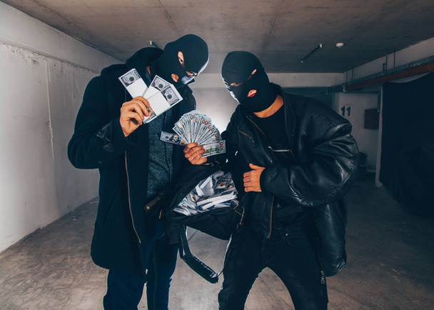 Терористы в масках забирают украденные деньги из черного мешка
 - Фото, изображение