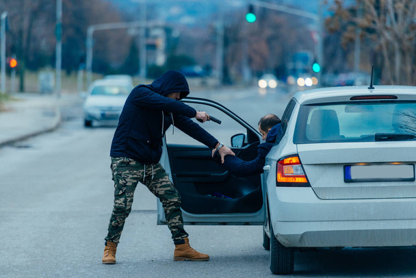 O ladrão de carros está puxando o dono do carro para fora de seu carro e tentando pegar o carro enquanto aponta uma arma carregada para a cabeça dos motoristas
. - Foto, Imagem