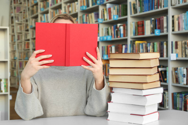 Молодая женщина читает книги за столом в библиотеке
 - Фото, изображение