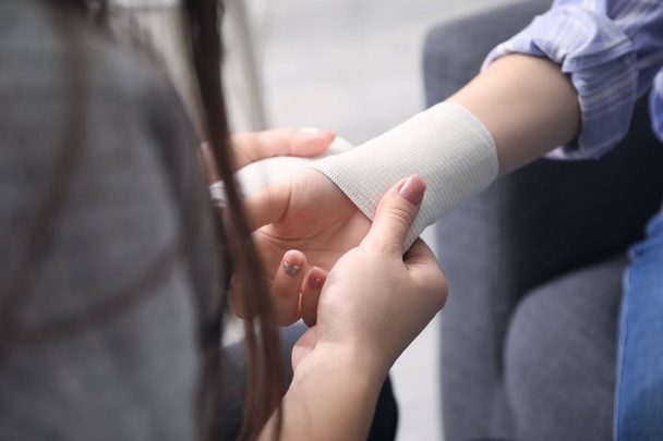 Woman applying bandage onto female wrist, closeup - Photo, Image