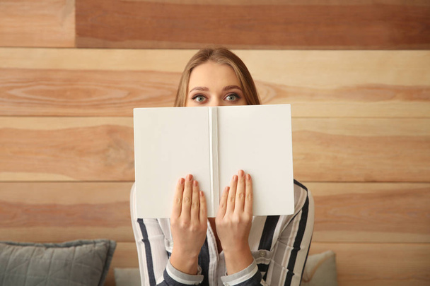 Mooie jonge vrouw met een boek in de buurt van houten muur - Foto, afbeelding