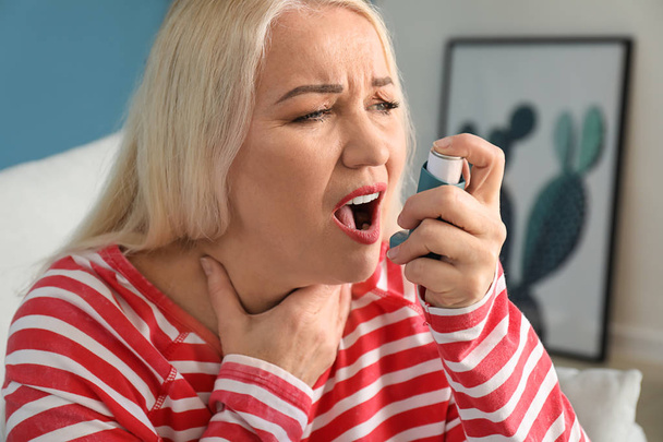 Зрелая женщина с ингалятором, у которой приступ астмы дома - Фото, изображение