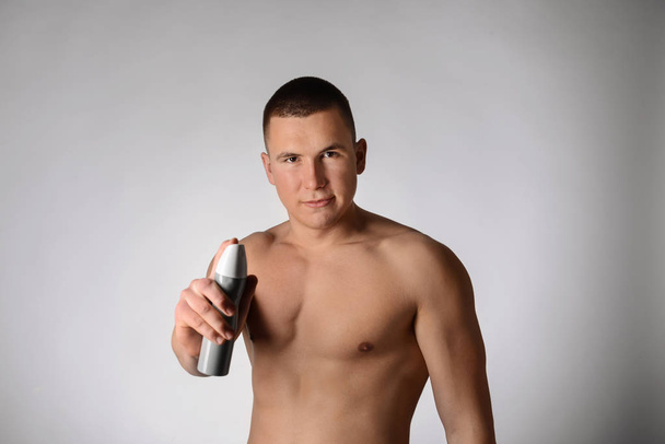 Joven guapo con desodorante sobre fondo gris
 - Foto, imagen