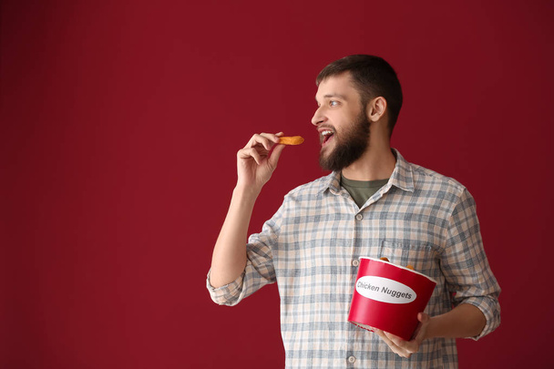 Handsome man with bucket of tasty nuggets on color background - Фото, изображение