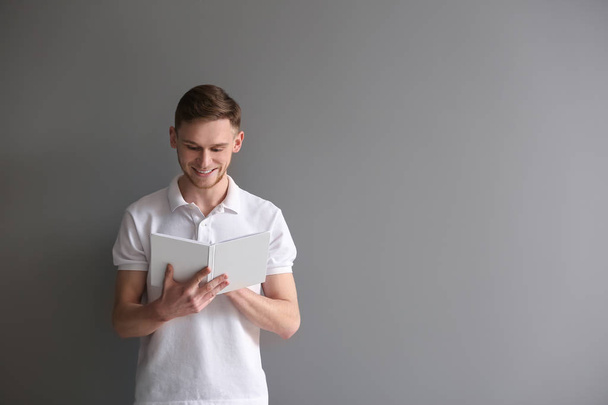 Handsome young man with book on grey background - Fotoğraf, Görsel