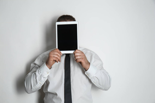 Businessman hiding face behind tablet computer on light background - Foto, imagen