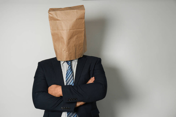 Empresario con bolsa de papel en la cabeza contra fondo claro
 - Foto, Imagen
